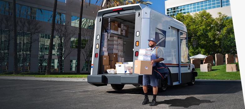 Letter carrier ready to deliver packages unloaded from the back of a USPS Next-Generation Delivery Vehicle.