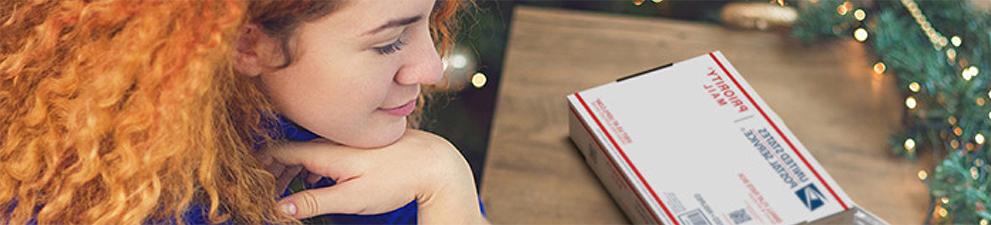 Woman on laptop with Priority Mail box and printed shipping label on the table next to her.